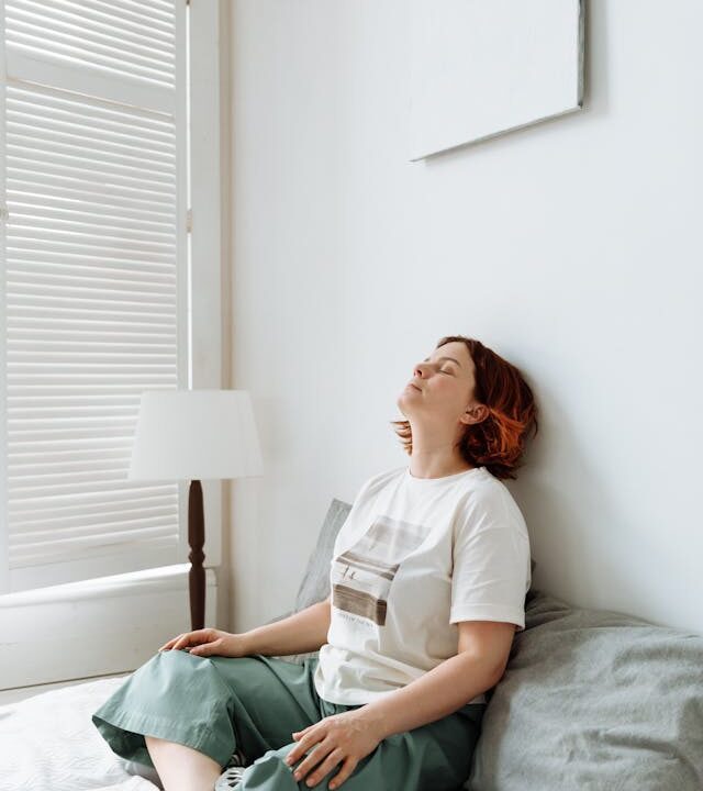 Yound woman sitting cross-legged on her bed with eyes closed
